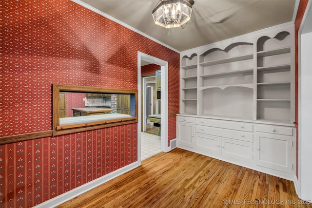 interior space with white cabinetry, light hardwood / wood-style floors, a notable chandelier, crown molding, and built in shelves