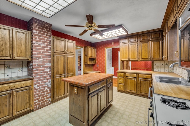 kitchen featuring ceiling fan, white range with gas stovetop, sink, and a center island