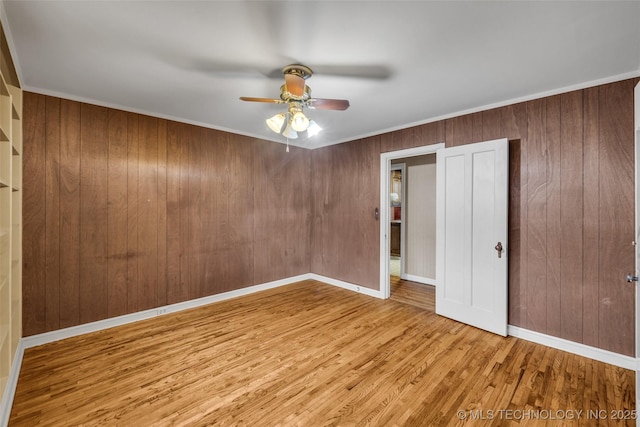 unfurnished bedroom featuring ceiling fan, hardwood / wood-style floors, crown molding, and wood walls