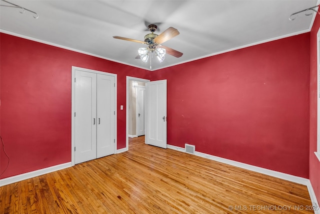 unfurnished bedroom featuring ceiling fan, light wood-type flooring, a closet, and crown molding