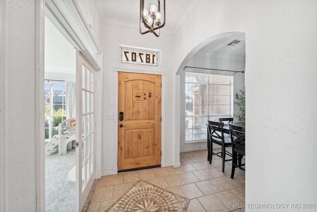 foyer featuring light tile patterned floors, visible vents, arched walkways, an inviting chandelier, and crown molding