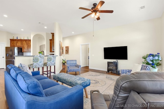 living room with light hardwood / wood-style flooring, ceiling fan, and a wood stove