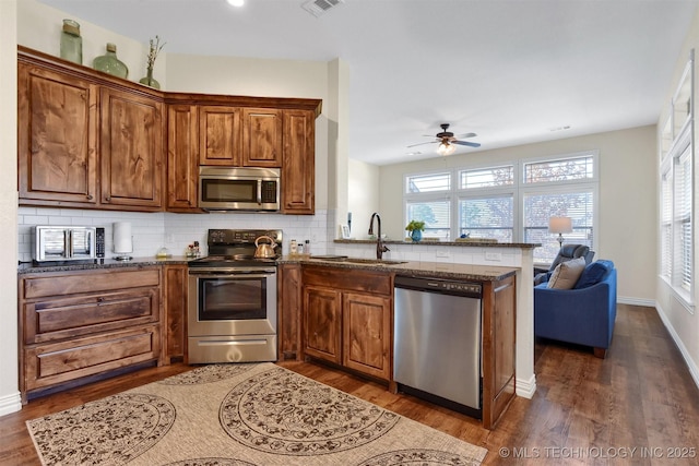 kitchen featuring appliances with stainless steel finishes, tasteful backsplash, sink, dark hardwood / wood-style flooring, and kitchen peninsula