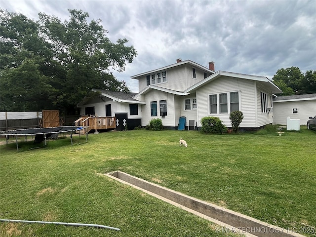 back of house with a wooden deck, a trampoline, a chimney, and a yard