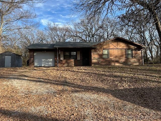 ranch-style house featuring dirt driveway, a shed, brick siding, and a garage