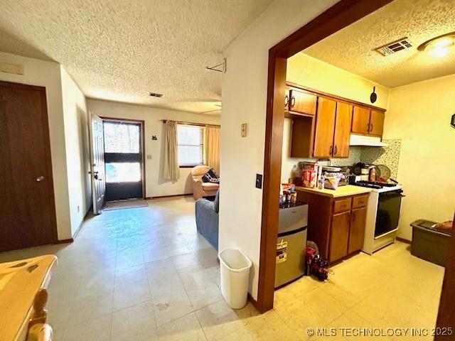 kitchen with under cabinet range hood, white range with gas stovetop, open floor plan, light countertops, and brown cabinets