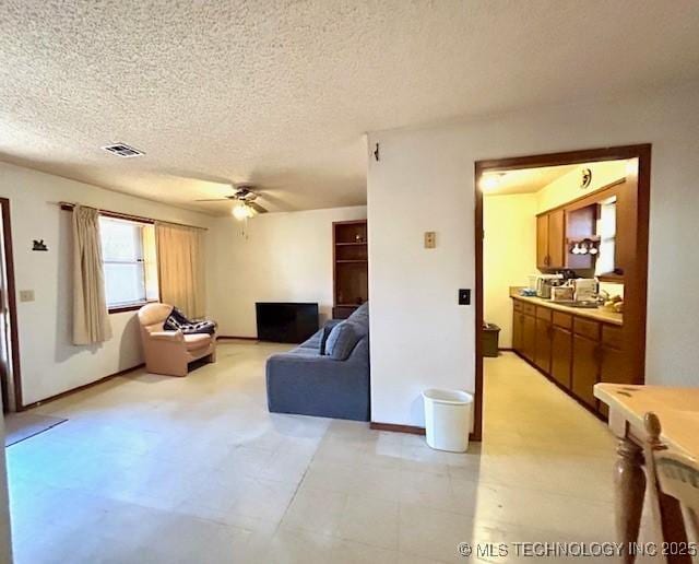 living area featuring a textured ceiling, ceiling fan, visible vents, and baseboards