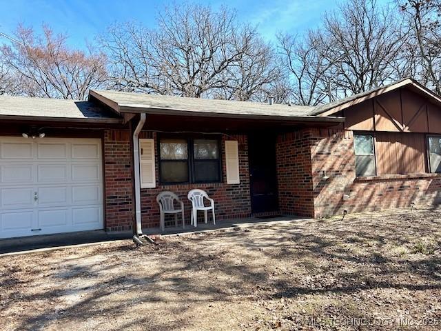 view of front of home featuring brick siding, dirt driveway, and an attached garage