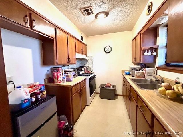 kitchen with visible vents, electric range oven, brown cabinets, light countertops, and a sink