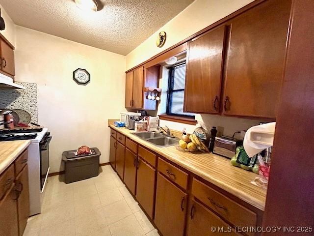 kitchen featuring stove, brown cabinets, light countertops, a textured ceiling, and a sink