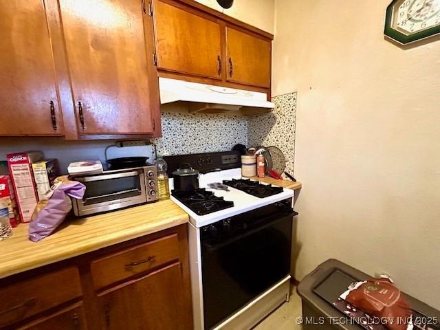 kitchen with brown cabinets, light countertops, under cabinet range hood, backsplash, and gas stove