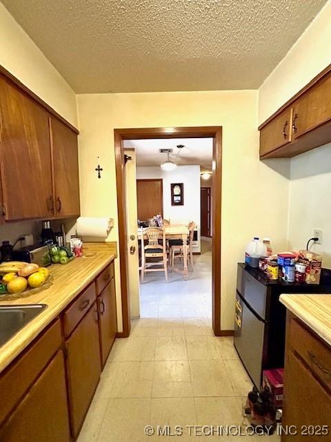 kitchen featuring a textured ceiling, a sink, light countertops, freestanding refrigerator, and brown cabinets