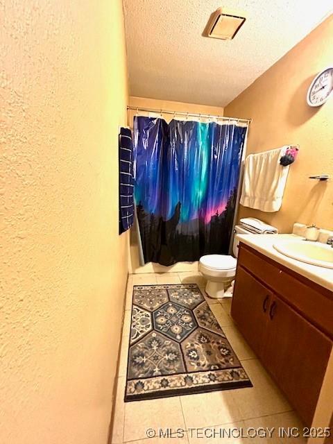 bathroom with a textured ceiling, a textured wall, toilet, vanity, and tile patterned floors