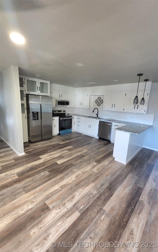 kitchen with kitchen peninsula, appliances with stainless steel finishes, white cabinets, dark hardwood / wood-style floors, and hanging light fixtures