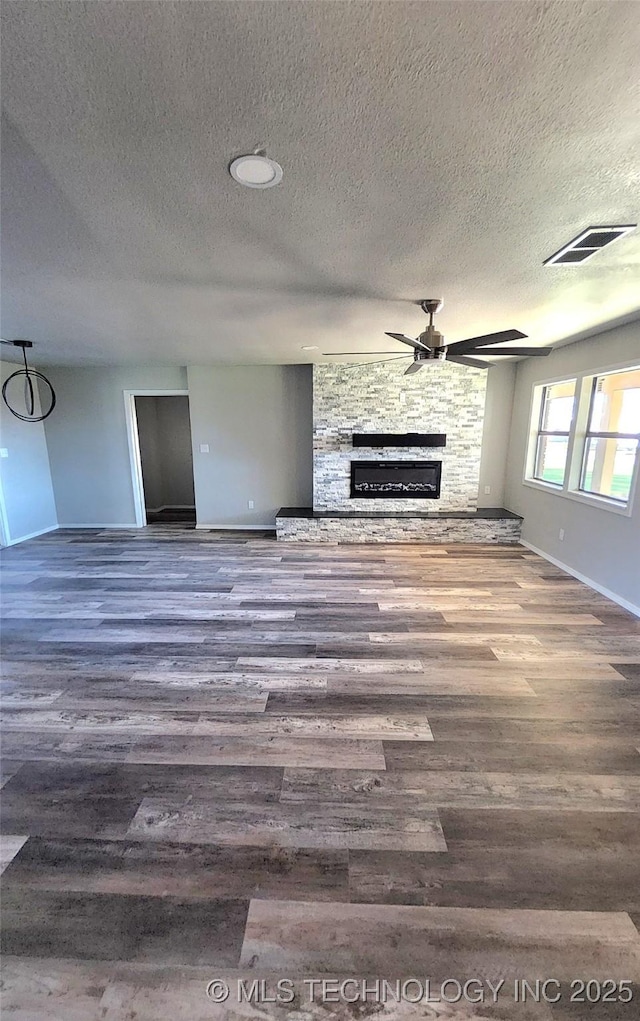 unfurnished living room featuring a stone fireplace, dark hardwood / wood-style flooring, and a textured ceiling