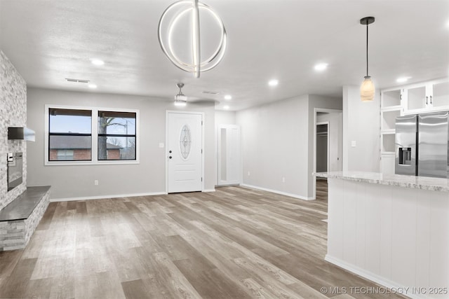 unfurnished living room featuring light wood-type flooring, visible vents, a stone fireplace, and baseboards