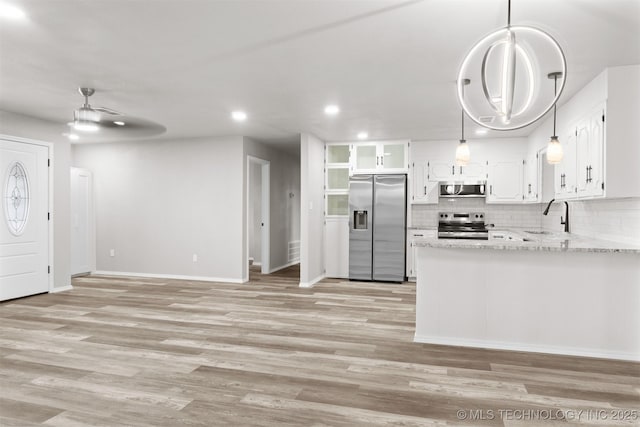 kitchen with light wood finished floors, stainless steel appliances, tasteful backsplash, white cabinetry, and a sink