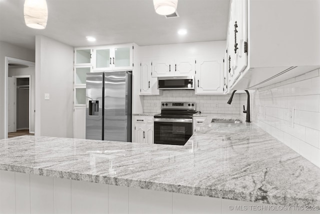 kitchen with visible vents, white cabinets, light stone countertops, stainless steel appliances, and a sink