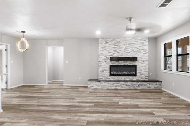 unfurnished living room featuring baseboards, visible vents, wood finished floors, and a stone fireplace