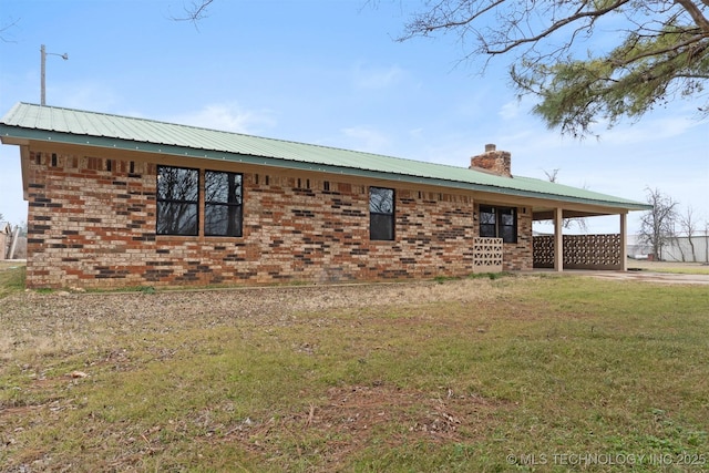 view of side of property with a carport, brick siding, a yard, and a chimney