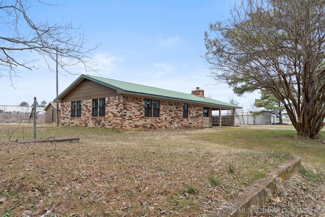 view of side of property with a chimney, fence, a lawn, and brick siding