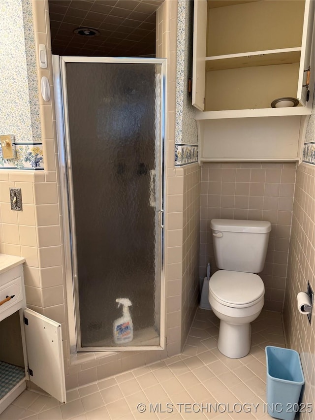 bathroom featuring tile patterned floors, toilet, a shower with shower door, tile walls, and vanity