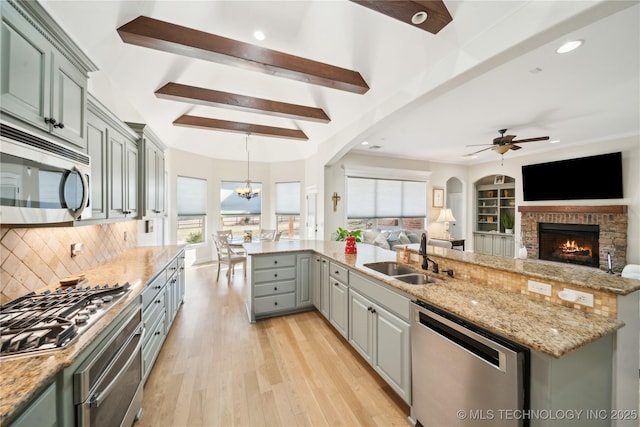 kitchen with ceiling fan with notable chandelier, sink, a fireplace, appliances with stainless steel finishes, and beam ceiling