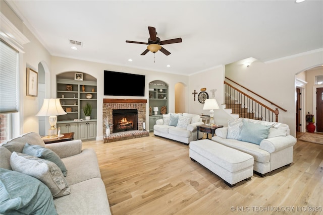 living room featuring crown molding, light hardwood / wood-style flooring, a brick fireplace, built in shelves, and ceiling fan