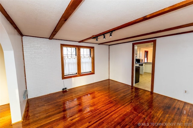 empty room featuring wood-type flooring, a textured ceiling, brick wall, and track lighting