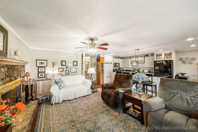 living room with a textured ceiling, a stone fireplace, ceiling fan, and crown molding