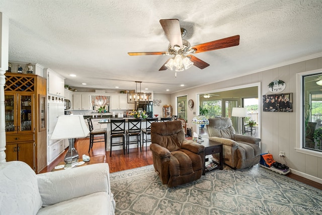 living room featuring hardwood / wood-style flooring, ceiling fan with notable chandelier, crown molding, and a textured ceiling