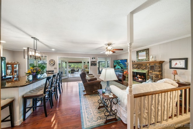 living room featuring a stone fireplace, dark hardwood / wood-style flooring, ceiling fan with notable chandelier, and ornamental molding