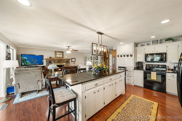 kitchen featuring black appliances, a kitchen bar, white cabinets, and hanging light fixtures