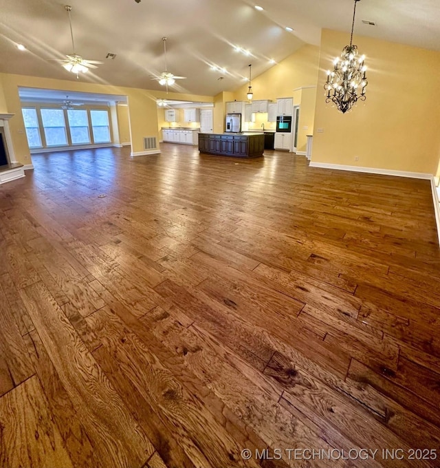 unfurnished living room with lofted ceiling, dark hardwood / wood-style flooring, and ceiling fan with notable chandelier