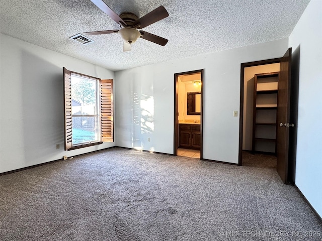 unfurnished bedroom with ensuite bathroom, a textured ceiling, ceiling fan, a spacious closet, and carpet floors