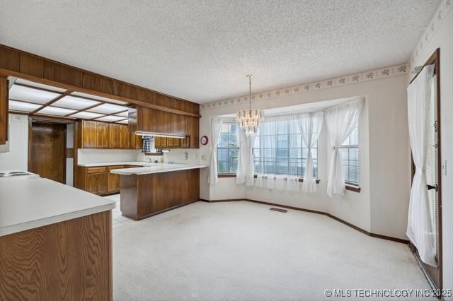 kitchen featuring light carpet, a textured ceiling, decorative light fixtures, kitchen peninsula, and a chandelier