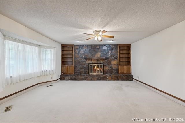 unfurnished living room with built in shelves, ceiling fan, a fireplace, and a textured ceiling