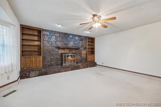 unfurnished living room with built in shelves, a textured ceiling, carpet floors, and a stone fireplace