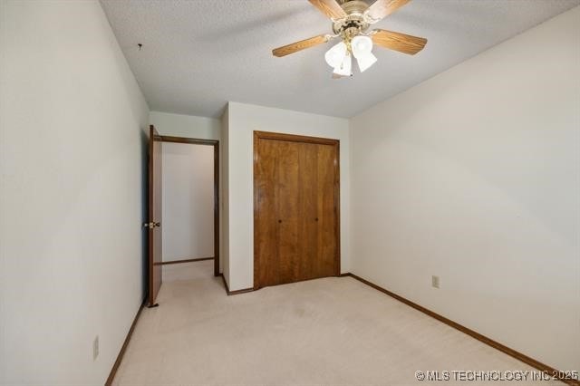 unfurnished bedroom featuring a textured ceiling, light colored carpet, a closet, and ceiling fan