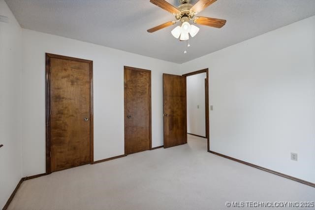 unfurnished bedroom with ceiling fan, light carpet, and two closets