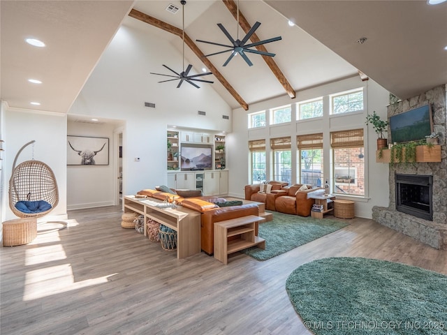 living room with light wood-type flooring, ceiling fan, beam ceiling, high vaulted ceiling, and a stone fireplace