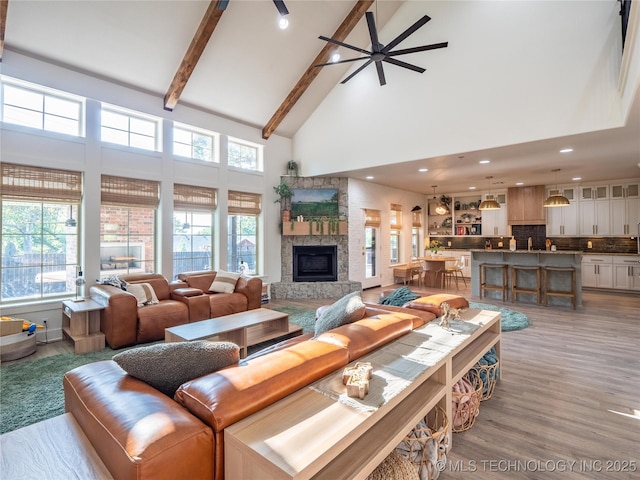 living room featuring high vaulted ceiling, a stone fireplace, ceiling fan, light hardwood / wood-style floors, and beam ceiling