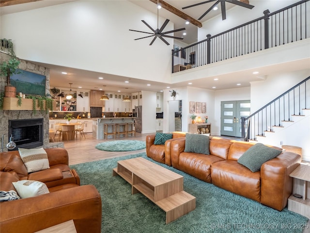 living room featuring a high ceiling, hardwood / wood-style flooring, ceiling fan, a fireplace, and beamed ceiling