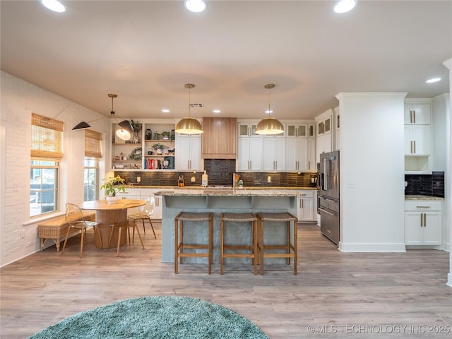 kitchen with pendant lighting, light wood-type flooring, a center island with sink, and white cabinetry