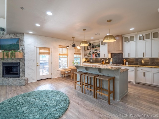 kitchen with pendant lighting, light hardwood / wood-style floors, a center island with sink, and white cabinetry