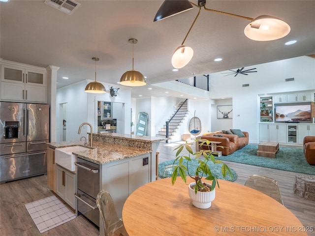 kitchen with sink, stainless steel refrigerator with ice dispenser, hanging light fixtures, an island with sink, and white cabinetry