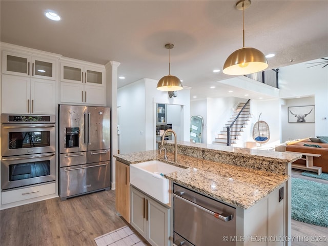 kitchen with sink, an island with sink, appliances with stainless steel finishes, decorative light fixtures, and white cabinetry