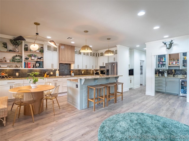 kitchen featuring wine cooler, stainless steel fridge, an island with sink, light hardwood / wood-style floors, and decorative light fixtures