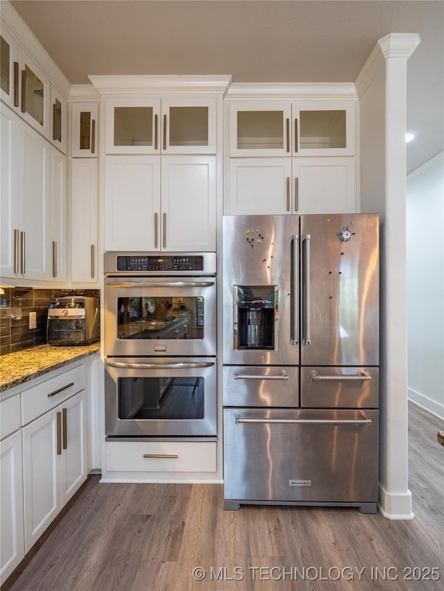 kitchen with white cabinets, decorative backsplash, appliances with stainless steel finishes, light stone counters, and wood-type flooring