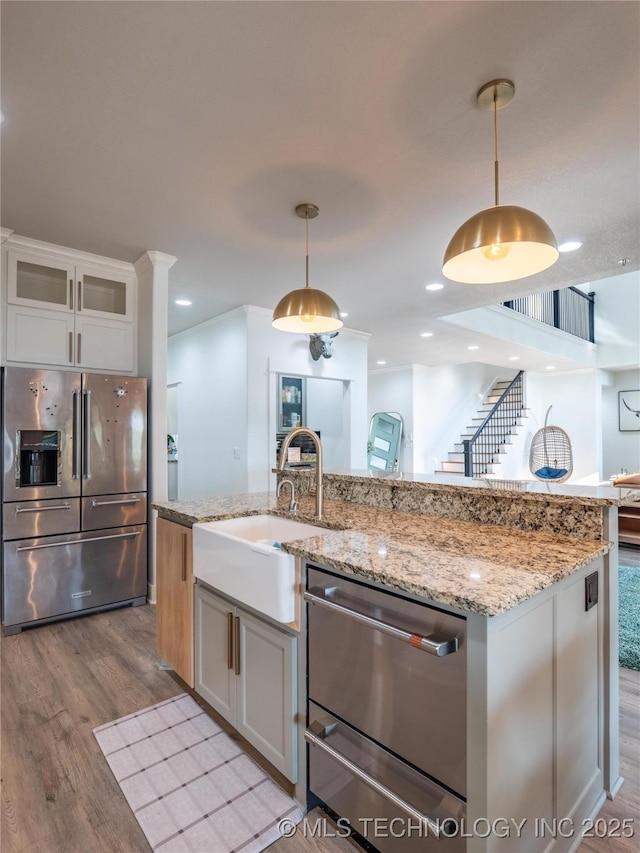 kitchen with stainless steel refrigerator with ice dispenser, light wood-type flooring, a kitchen island with sink, decorative light fixtures, and white cabinets